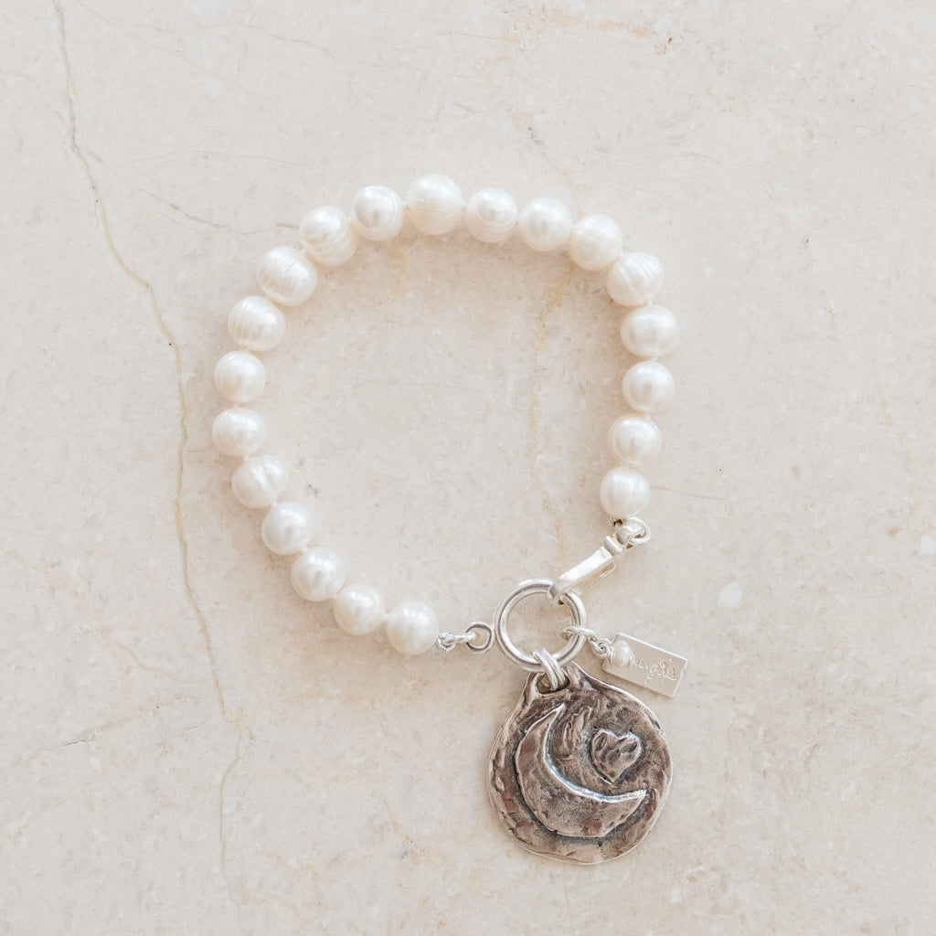 Elegant Abigail pearl bracelet featuring a sterling silver heart and moon disc charm, designed as a love token by Pearly Girls. The bracelet showcases lustrous pearls strung together, complemented by the delicately crafted heart and moon charms, symbolizing love and affection