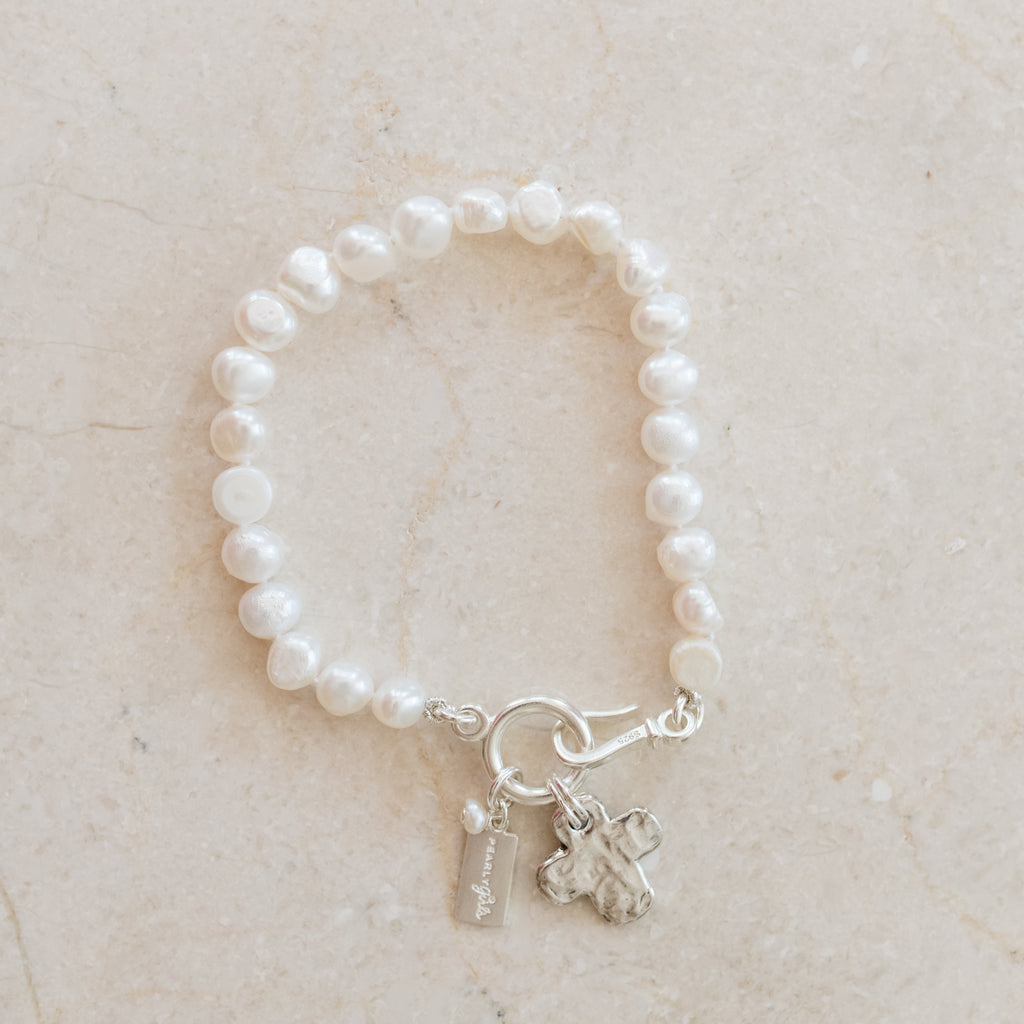 Lanie Pearl Bracelet by Pearly Girls, featuring white freshwater pearls and a sterling silver hammered cross. This bracelet combines the timeless elegance of white pearls with a distinctive sterling silver cross, showcasing a hammered texture for a unique and meaningful accessory.