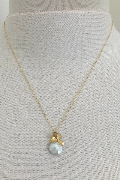 Orchid Pearl Necklace by Pearly Girls, featuring a freshwater coin pearl and a gold orchid pendant. This necklace beautifully combines the broad, lustrous surface of a coin pearl with an intricately designed gold orchid pendant, creating a piece that is both elegant and botanical in inspiration.