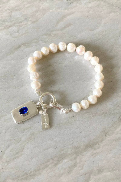 Charlotte Pearl Bracelet by Pearly Girls, adorned with a sapphire charm and freshwater pearls. This bracelet elegantly pairs the rich, deep blue of the sapphire with the classic luster of freshwater pearls, creating a luxurious and eye-catching piece.