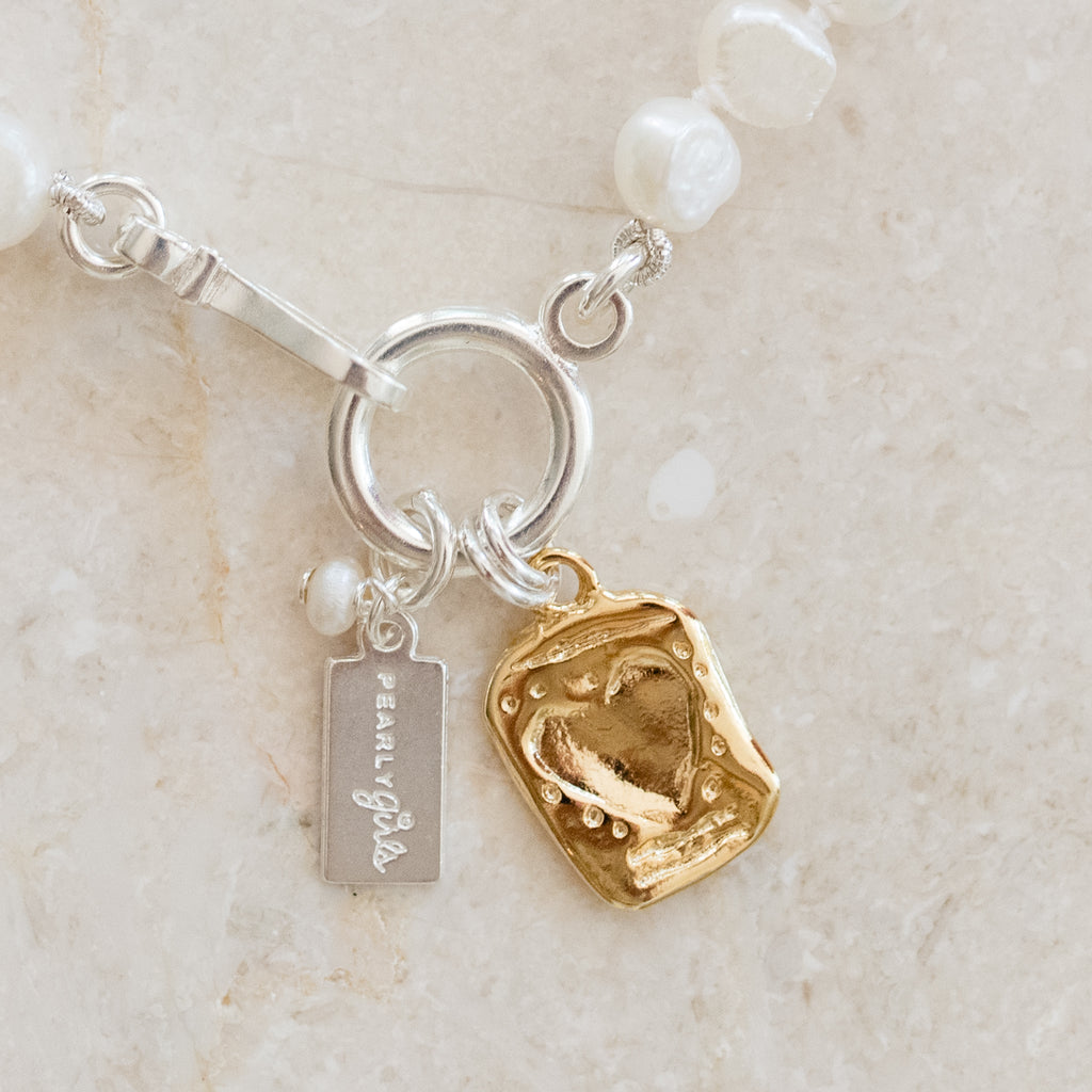 Rachel Pearl Bracelet by Pearly Girls, featuring a gold etched heart and freshwater pearls. This bracelet elegantly combines the classic charm of freshwater pearls with a gold etched heart, adding a romantic and personal touch to the timeless beauty of pearl jewelry.