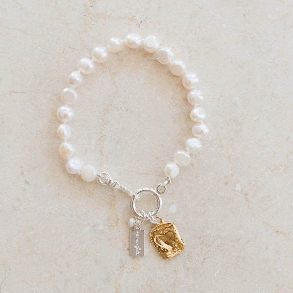 Rachel Pearl Bracelet by Pearly Girls, featuring a gold etched heart and freshwater pearls. This bracelet elegantly combines the classic charm of freshwater pearls with a gold etched heart, adding a romantic and personal touch to the timeless beauty of pearl jewelry.