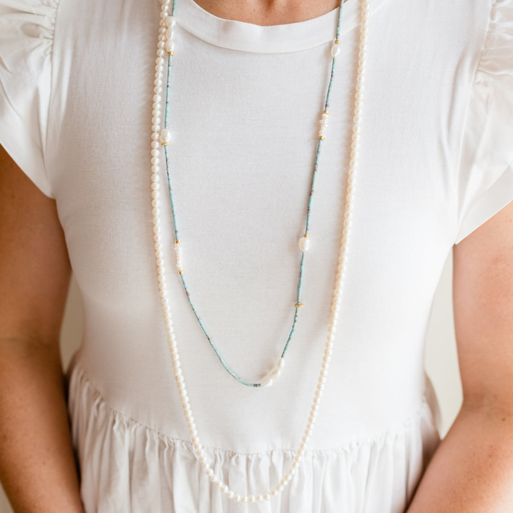 Jess Turquoise and Pearl Necklace by Pearly Girls, a long artisan elegance turquoise necklace with gold accents. This necklace artfully blends vibrant turquoise beads with classic pearls, highlighted by touches of gold, creating a piece that exudes both the richness of artisan craftsmanship and the timeless beauty of mixed materials.