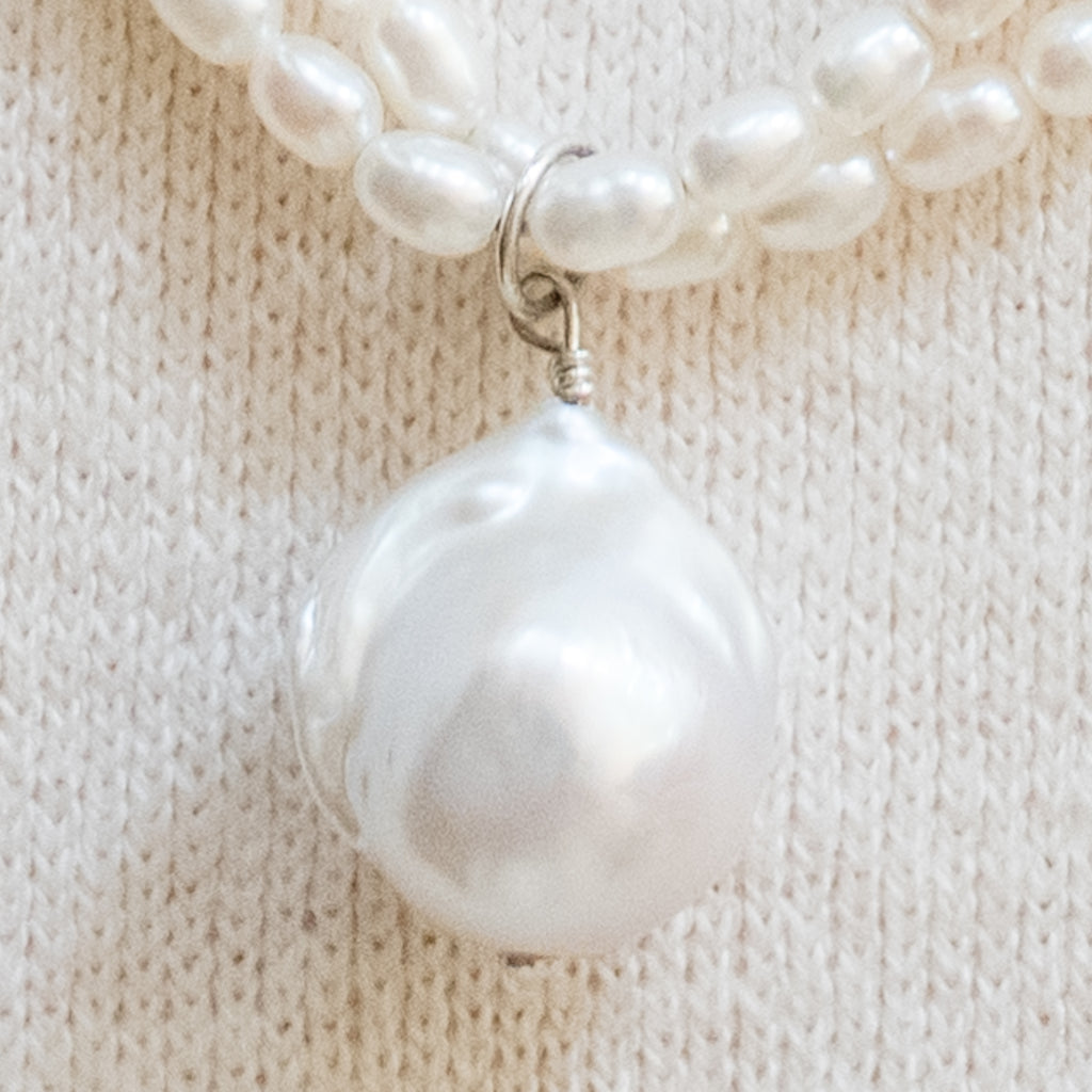 Claire Pearl Necklace by Pearly Girls features a fireball pearl pendant and seed pearls. This necklace elegantly showcases a striking fireball pearl pendant, complemented by a string of delicate seed pearls, creating a balance of boldness and subtlety in its design.