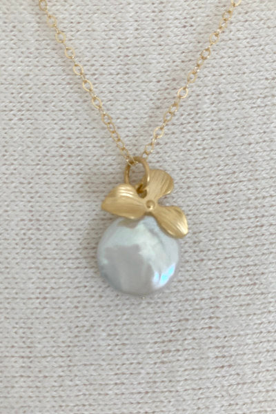 Orchid Pearl Necklace by Pearly Girls, featuring a freshwater coin pearl and a gold orchid pendant. This necklace beautifully combines the broad, lustrous surface of a coin pearl with an intricately designed gold orchid pendant, creating a piece that is both elegant and botanical in inspiration.