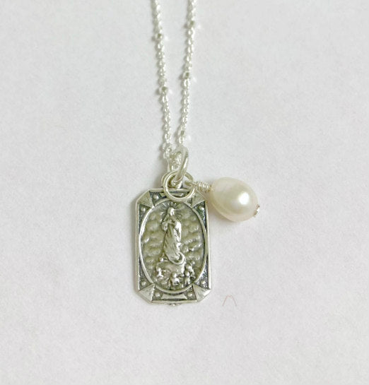 Mary Pearl Necklace by Pearly Girls, featuring a sterling silver Saint tag and freshwater pearl. This necklace combines the spiritual symbolism of a Saint tag in sterling silver with the timeless elegance of a freshwater pearl, creating a piece that is both meaningful and classically beautiful.