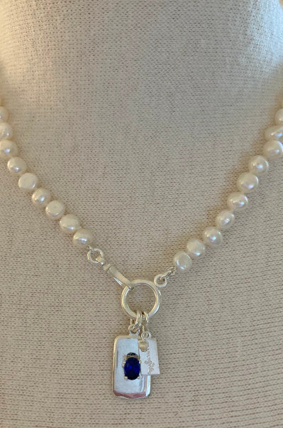 Charlotte Pearl Necklace by Pearly Girls, featuring a sapphire tag charm and lustrous pearls. This necklace beautifully combines the vibrant allure of a sapphire charm with the timeless elegance of pearls, creating a sophisticated and captivating accessory.