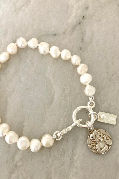 Rosie Pearl Bracelet by Pearly Girls, adorned with a cherub charm and freshwater pearls. This bracelet pairs the timeless elegance of pearls with a playful cherub charm, creating a whimsical and charming piece that combines classic beauty with a touch of angelic whimsy.