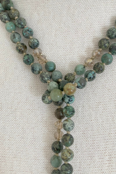 Turquoise Beaded Lariat Necklace by Pearly Girls, featuring smoky crystals and crystal tassels. This necklace elegantly combines vibrant turquoise beads with the subtle shimmer of smoky crystals, accented by sparkling crystal tassels, creating a piece that's both colorful and elegantly detailed.