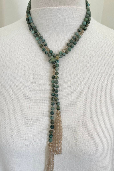 Turquoise Beaded Lariat Necklace by Pearly Girls, featuring smoky crystals and crystal tassels. This necklace elegantly combines vibrant turquoise beads with the subtle shimmer of smoky crystals, accented by sparkling crystal tassels, creating a piece that's both colorful and elegantly detailed.